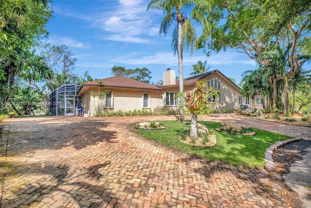 ranch-style home featuring decorative driveway, a chimney, stucco siding, a front yard, and a lanai