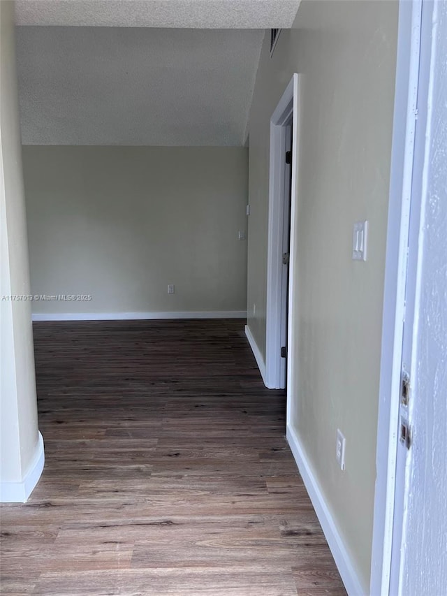 empty room with a textured ceiling, wood finished floors, visible vents, and baseboards