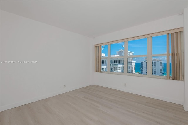 empty room with a city view, light wood-type flooring, and baseboards