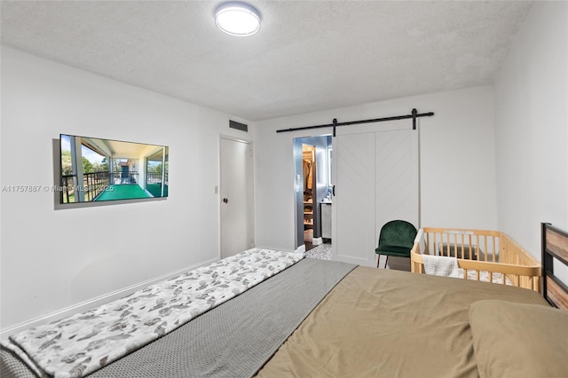 bedroom featuring a barn door, a textured ceiling, and visible vents