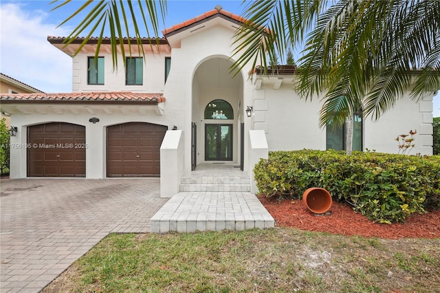 doorway to property featuring a tiled roof, decorative driveway, an attached garage, and stucco siding