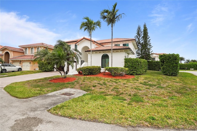 mediterranean / spanish home with a tile roof, stucco siding, a garage, driveway, and a front lawn