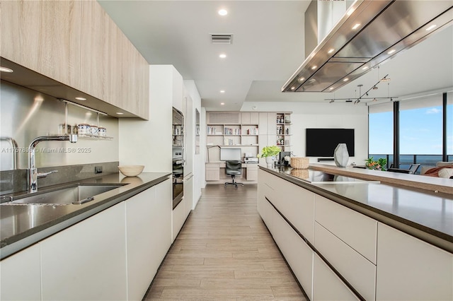 kitchen featuring light wood finished floors, visible vents, dark countertops, modern cabinets, and a sink