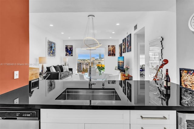 kitchen with dark countertops, open floor plan, white cabinets, a sink, and dishwasher