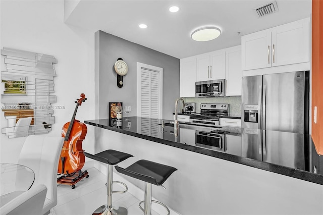 kitchen featuring a breakfast bar area, stainless steel appliances, visible vents, white cabinetry, and tasteful backsplash