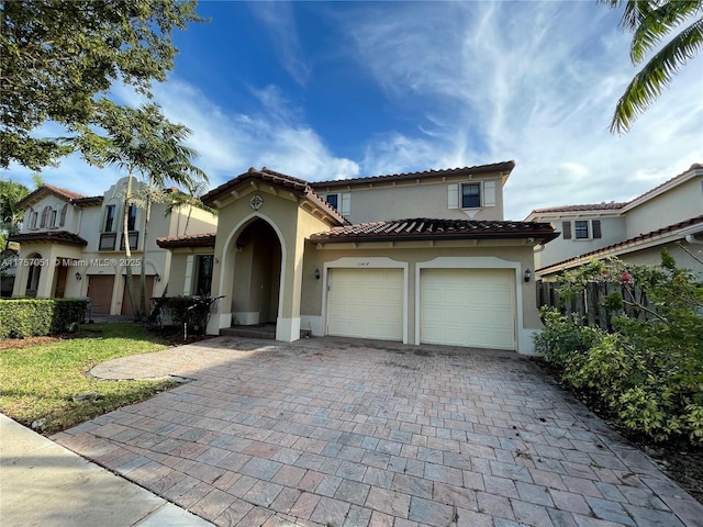 mediterranean / spanish house with decorative driveway, a tiled roof, an attached garage, and stucco siding