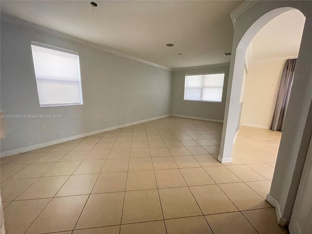 spare room with ornamental molding, arched walkways, baseboards, and light tile patterned floors