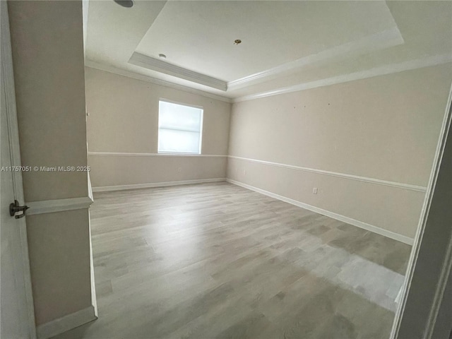 spare room with ornamental molding, wood finished floors, a raised ceiling, and baseboards