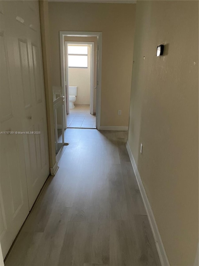 corridor featuring light wood finished floors and baseboards