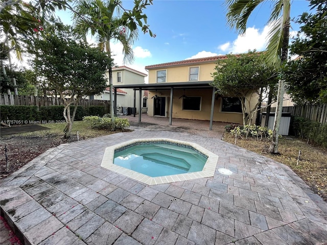 back of house with an in ground hot tub, fence, a patio, and stucco siding