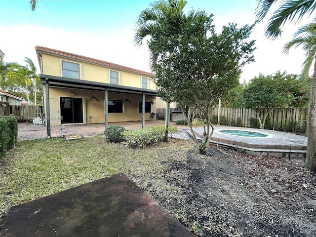 rear view of house featuring an outdoor hot tub, a fenced backyard, a patio, and stucco siding