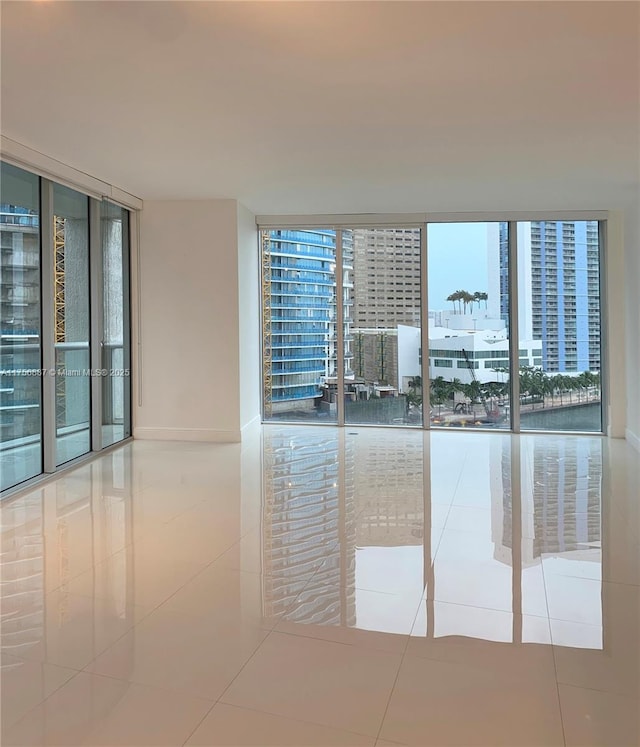 empty room with expansive windows, baseboards, and tile patterned floors