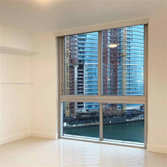 unfurnished room featuring a water view, baseboards, and tile patterned floors