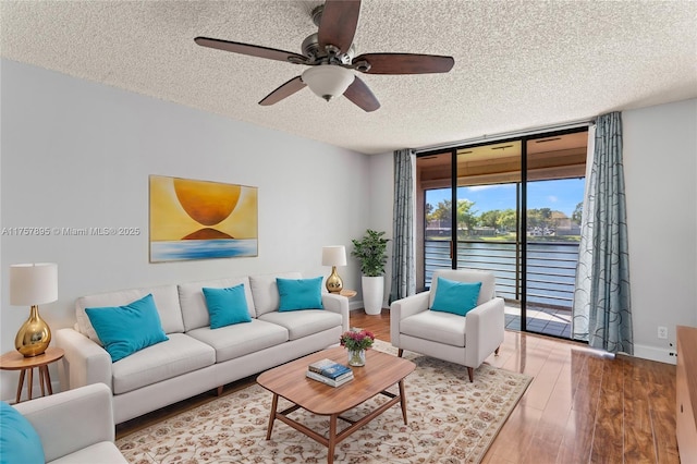 living area with a textured ceiling, a wall of windows, wood finished floors, and baseboards