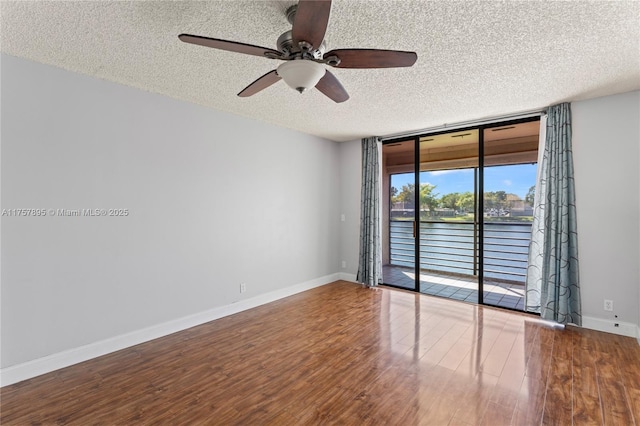 spare room with baseboards, ceiling fan, wood finished floors, expansive windows, and a textured ceiling