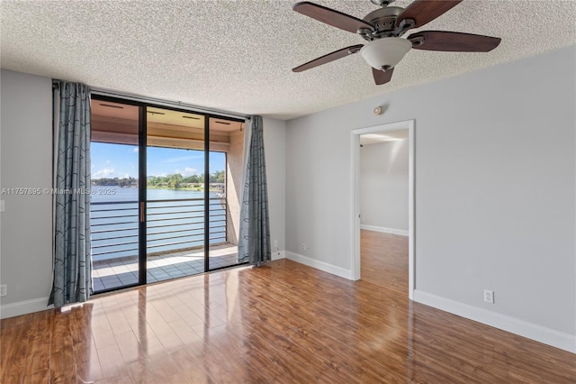 unfurnished room featuring a textured ceiling, a water view, wood finished floors, baseboards, and a wall of windows