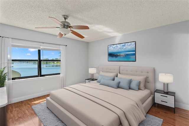 bedroom featuring a textured ceiling, wood finished floors, a ceiling fan, and baseboards