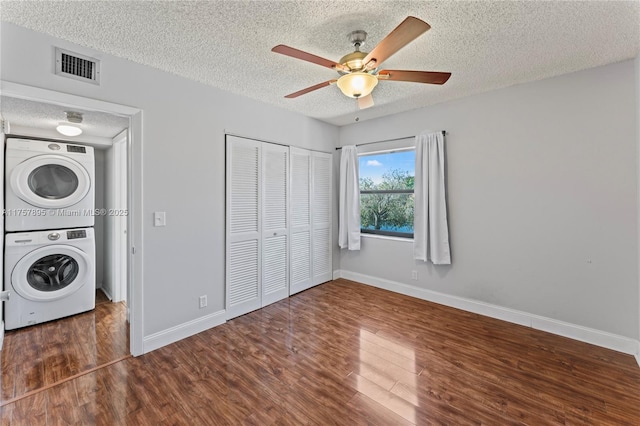 laundry area with laundry area, wood finished floors, visible vents, baseboards, and stacked washing maching and dryer