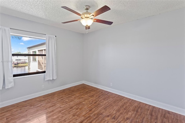 spare room featuring a textured ceiling, wood finished floors, a ceiling fan, and baseboards