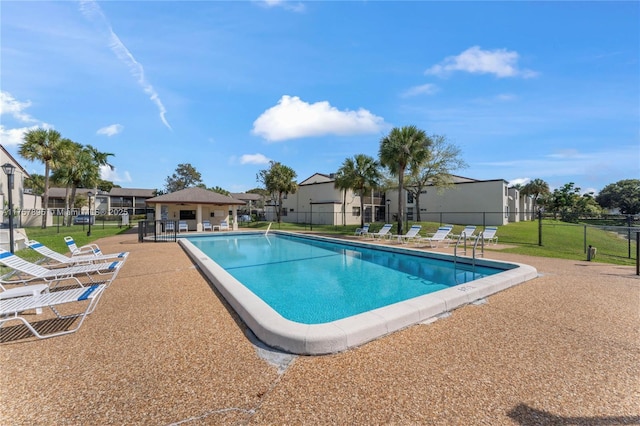 community pool with a patio, a lawn, fence, and a residential view