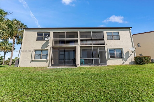 back of property with a sunroom, a lawn, a balcony, and stucco siding