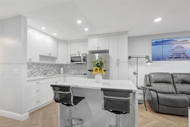 kitchen with white cabinetry, a kitchen breakfast bar, open floor plan, appliances with stainless steel finishes, and tasteful backsplash