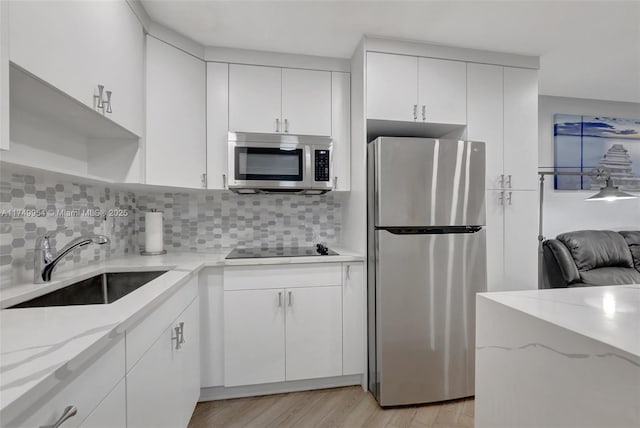 kitchen with stainless steel appliances, a sink, white cabinetry, and decorative backsplash