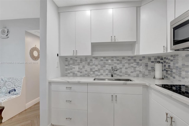 kitchen with black electric stovetop, tasteful backsplash, stainless steel microwave, white cabinetry, and a sink