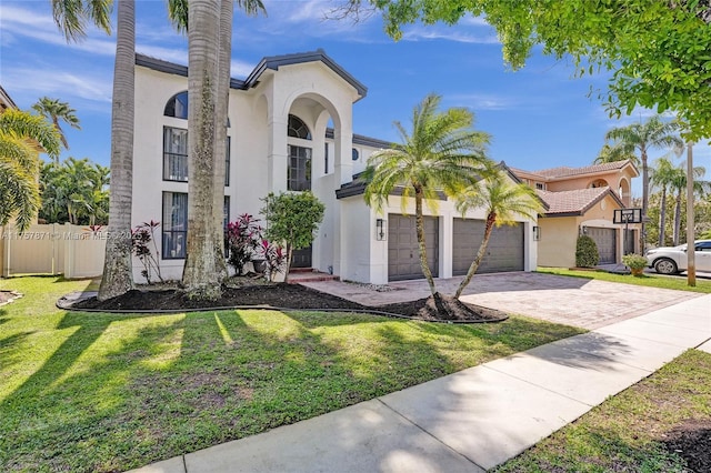 mediterranean / spanish house featuring a garage, fence, decorative driveway, stucco siding, and a front lawn