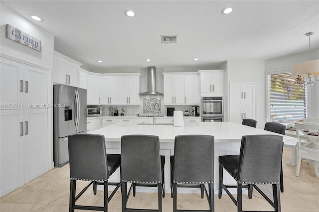 kitchen featuring a breakfast bar area, backsplash, appliances with stainless steel finishes, white cabinets, and wall chimney exhaust hood