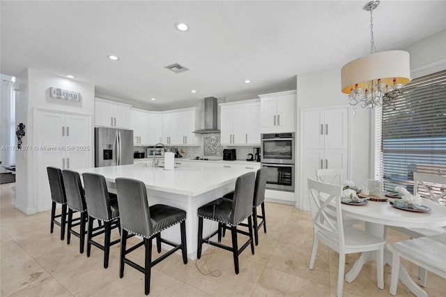 kitchen with a breakfast bar area, stainless steel appliances, visible vents, decorative backsplash, and wall chimney range hood