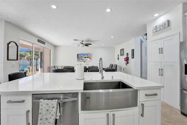 kitchen with white cabinets, open floor plan, light countertops, stainless steel dishwasher, and a sink