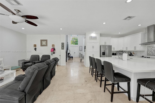 kitchen with open floor plan, wall chimney exhaust hood, stainless steel fridge, and visible vents