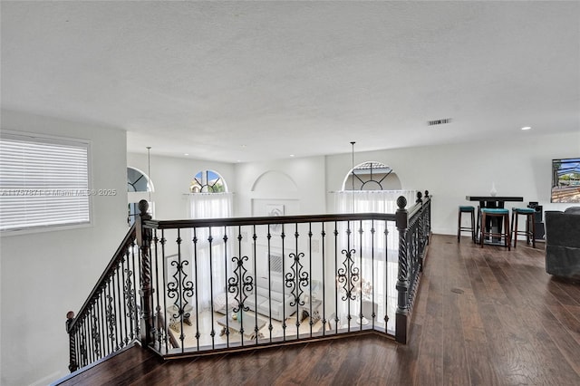 hall with a notable chandelier, visible vents, a textured ceiling, an upstairs landing, and wood finished floors