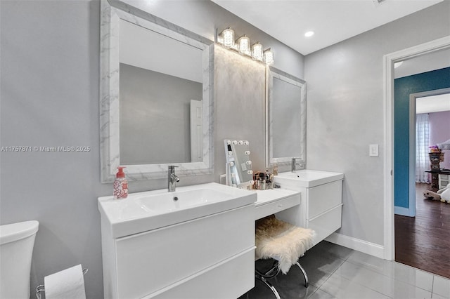 full bath with tile patterned flooring, toilet, a sink, two vanities, and baseboards