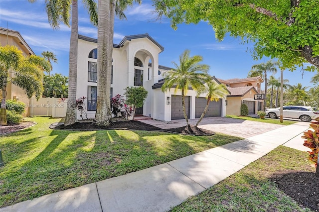 mediterranean / spanish-style home featuring an attached garage, fence, decorative driveway, stucco siding, and a front lawn