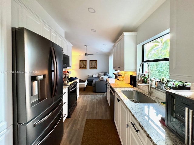 kitchen featuring black appliances, a sink, open floor plan, white cabinetry, and dark wood-style flooring