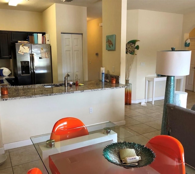 kitchen with light tile patterned floors, stainless steel fridge with ice dispenser, a peninsula, stone counters, and a sink