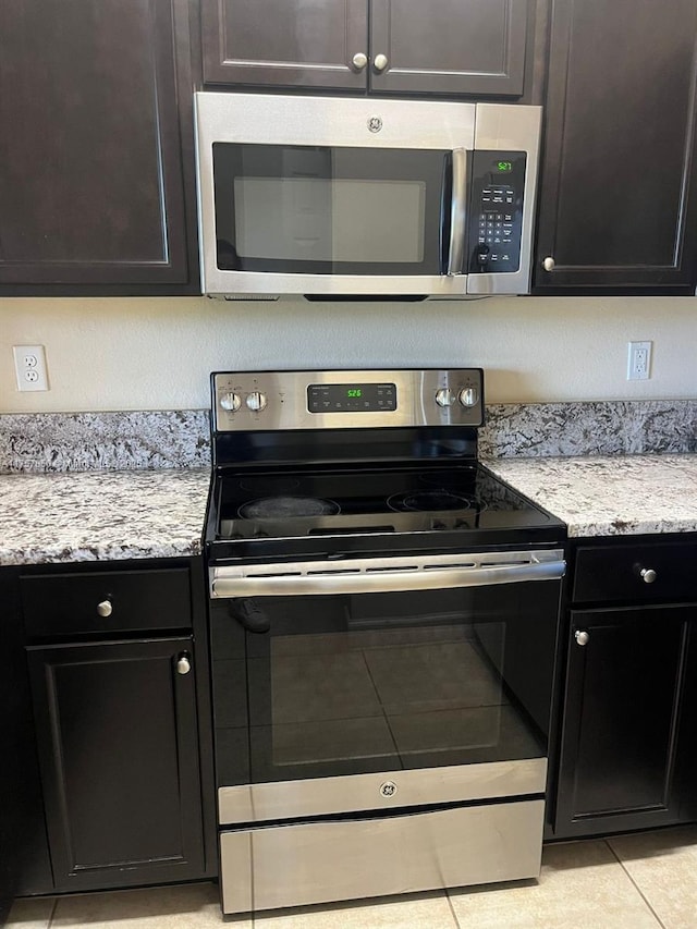 kitchen with stainless steel appliances, light tile patterned flooring, and light stone counters