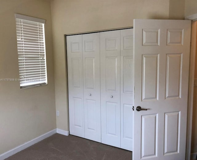 unfurnished bedroom with dark colored carpet, a closet, and baseboards