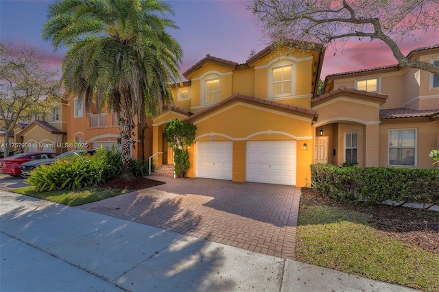 mediterranean / spanish house featuring decorative driveway, a tile roof, an attached garage, and stucco siding