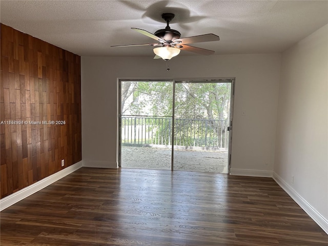 unfurnished room with a textured ceiling, wooden walls, and dark wood-type flooring