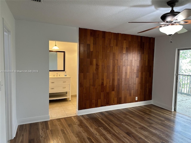 unfurnished bedroom featuring an accent wall, wood finished floors, a textured ceiling, wood walls, and a sink