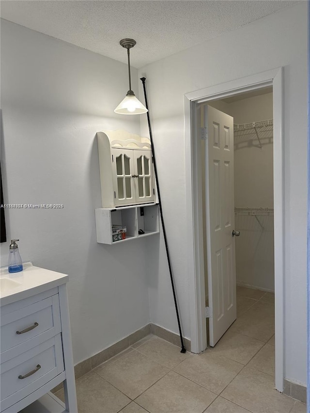 bathroom with tile patterned flooring, a walk in closet, a textured ceiling, and vanity