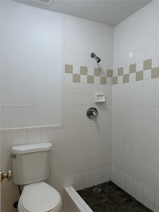 bathroom featuring toilet, a tile shower, and tile walls