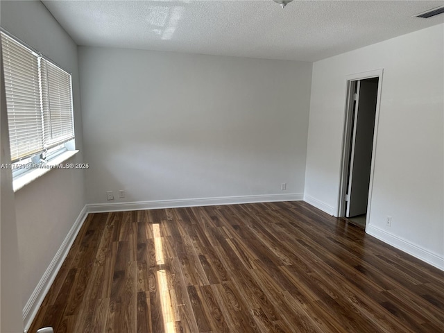 unfurnished room with dark wood-style floors, a textured ceiling, visible vents, and baseboards