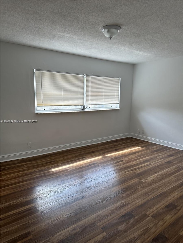 unfurnished room with dark wood-style flooring, a textured ceiling, and baseboards