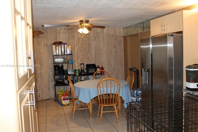 dining room with wood walls, a ceiling fan, a textured ceiling, and light tile patterned flooring