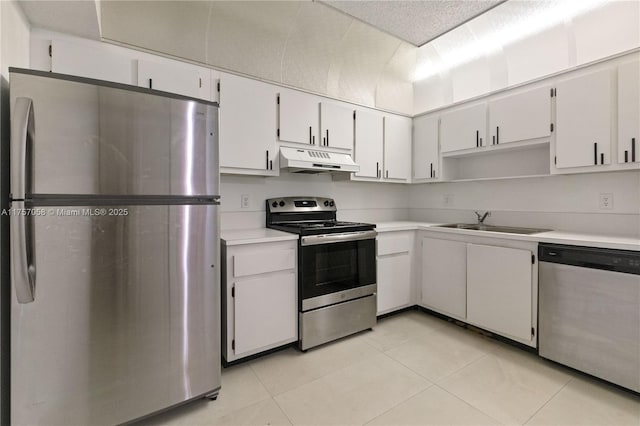 kitchen with appliances with stainless steel finishes, light countertops, under cabinet range hood, a sink, and light tile patterned flooring