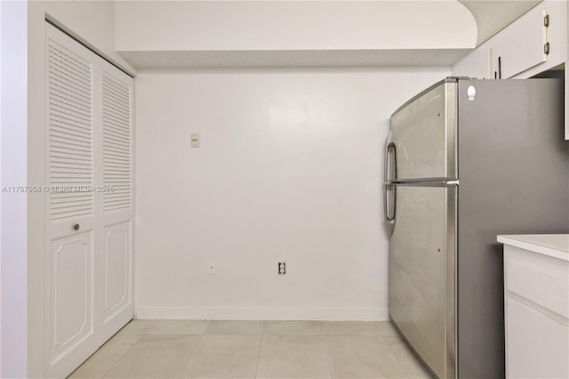 kitchen featuring light tile patterned flooring, white cabinetry, baseboards, light countertops, and freestanding refrigerator